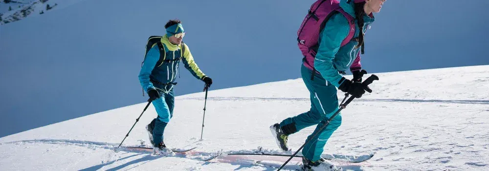 Två skidåkare med skinnbelagda skidor går uppför fjäll