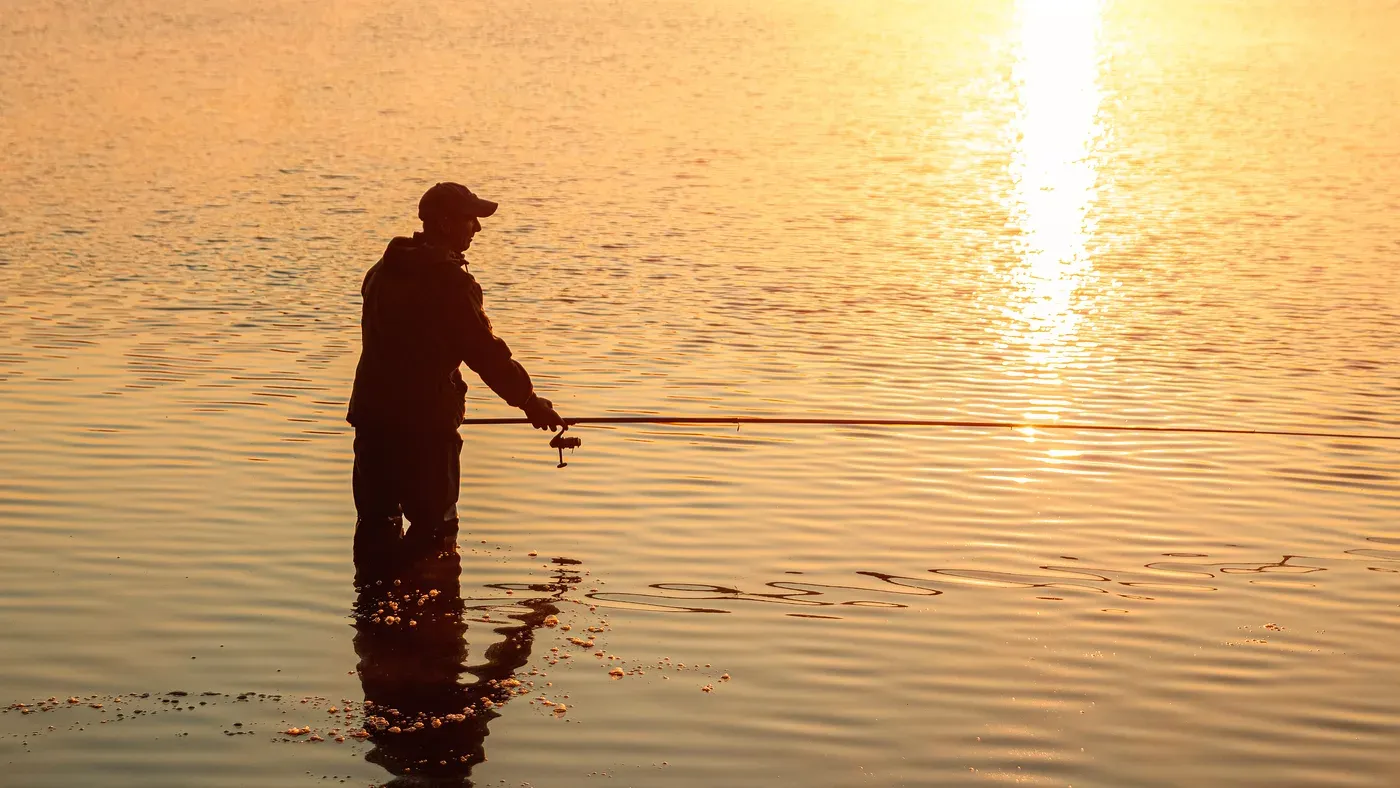 Fiskare i keps med spö i motljus vid vattnet