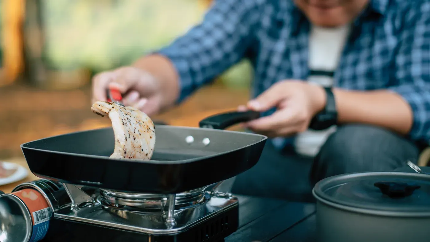 Man steker kött i stekpanna på gasolkök utomhus