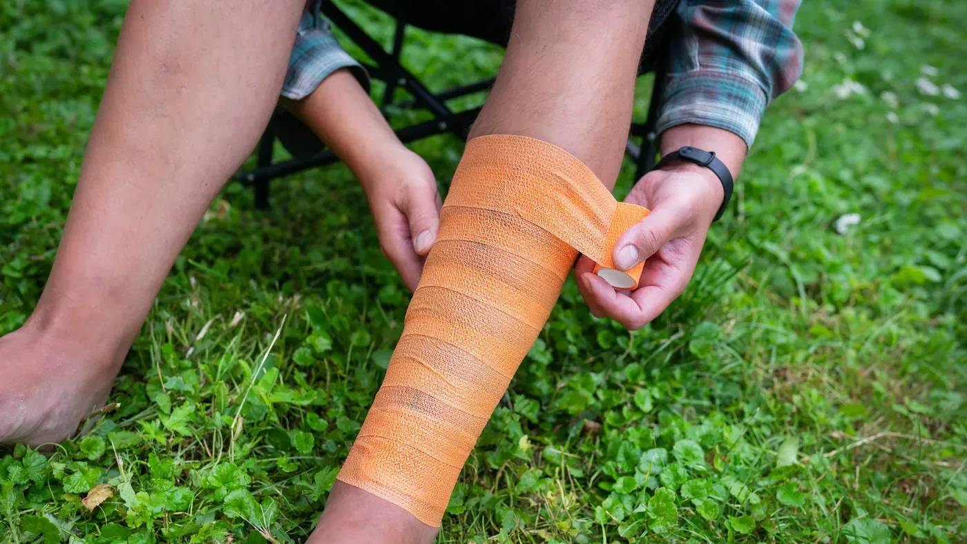 Person lindar orange elastisk bandage runt underben på gräsmatta