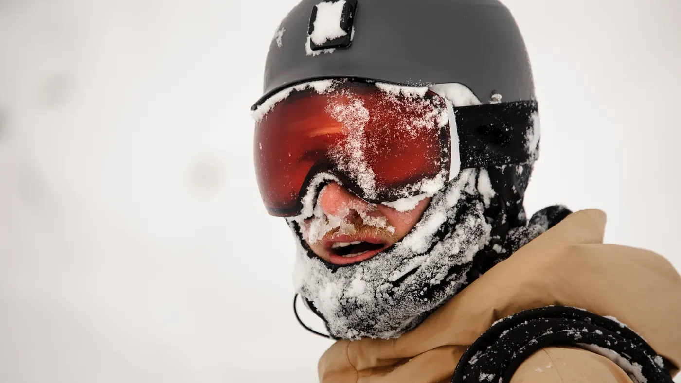 Snötäckt ansikte med grå hjälm och röda skidglasögon