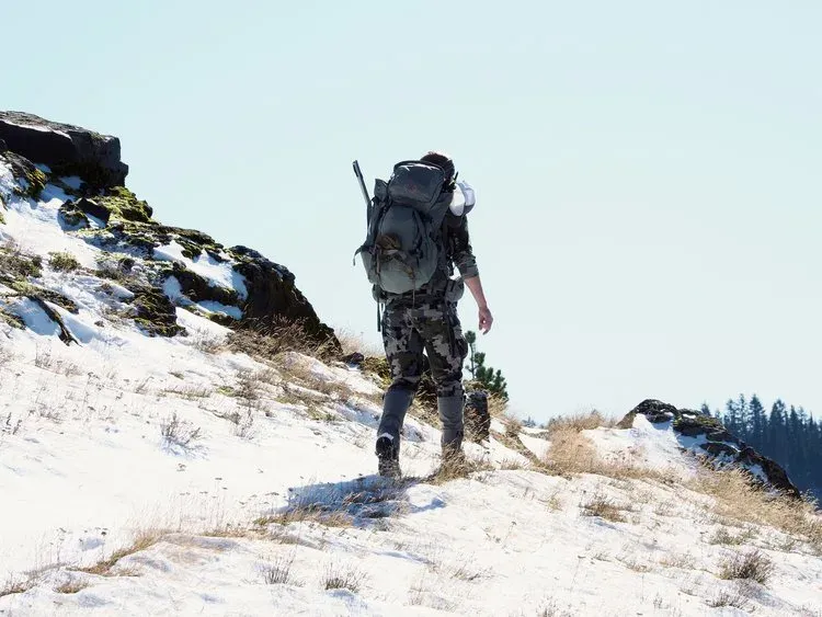Jägare med ryggsäck och gevär vandrar på snötäckt bergsrygg