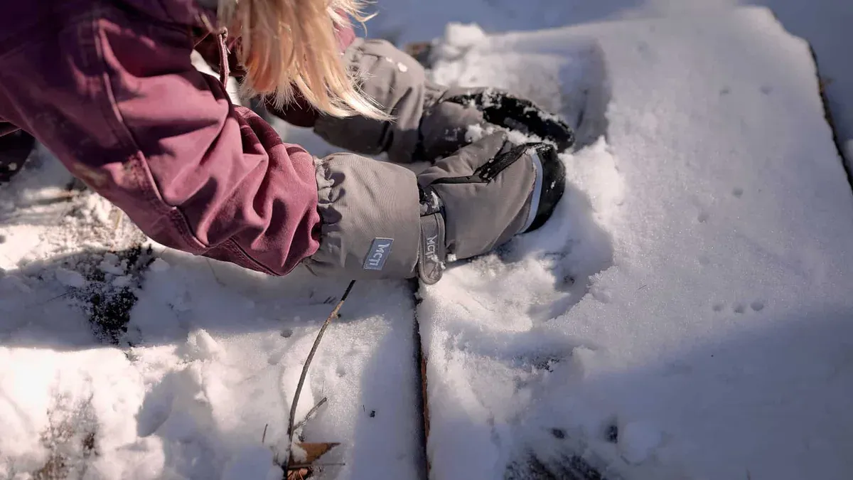 Barns hand i grå vante i snön