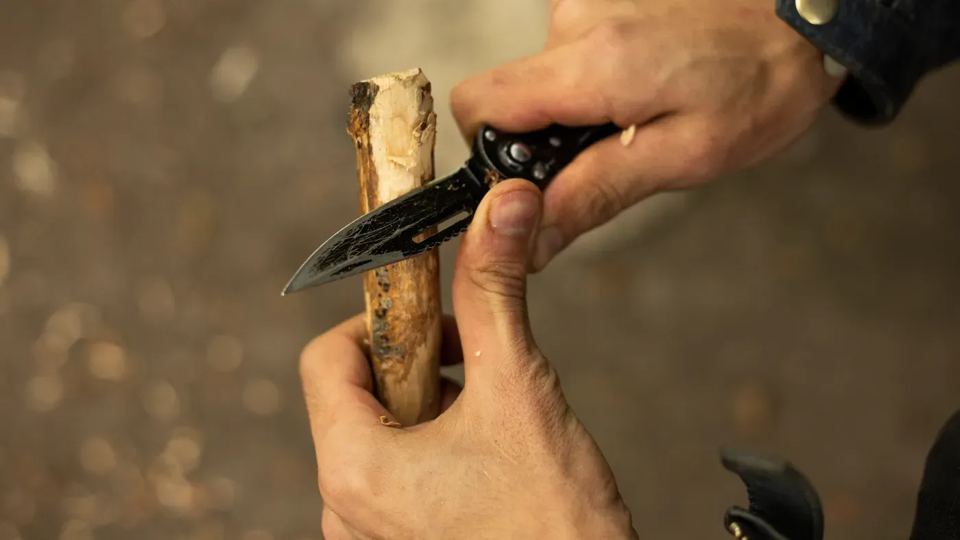 Händer täljer en pinne med svart fällkniv
