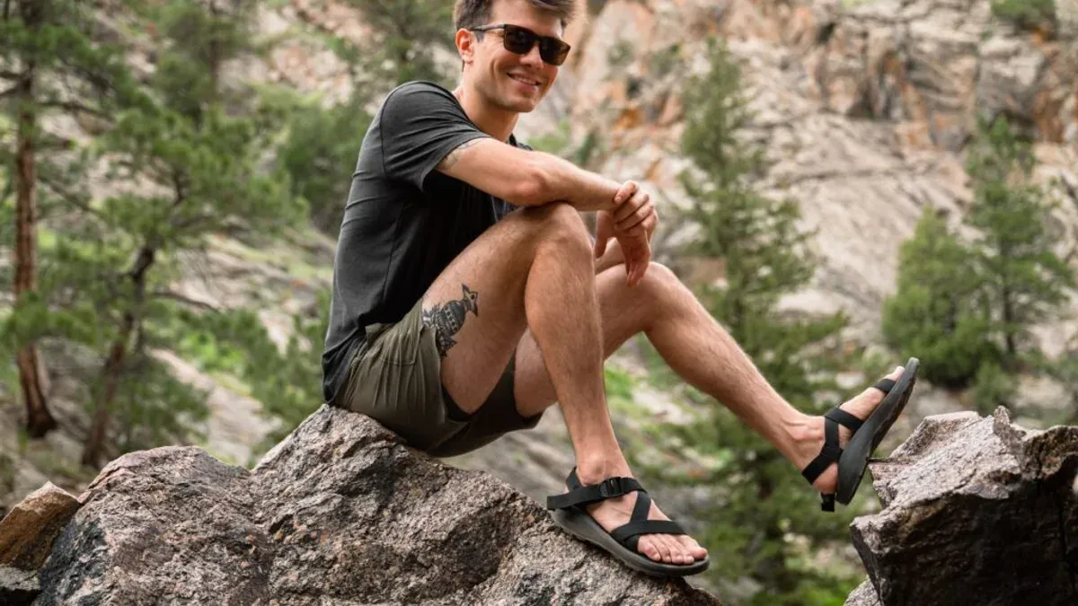 Man i sandaler sitter leende på klippa i naturen