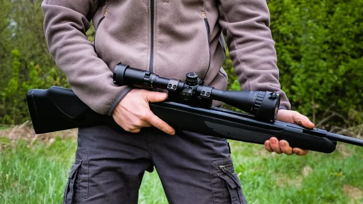 Man håller svart luftgevär med kikarsikte i famnen