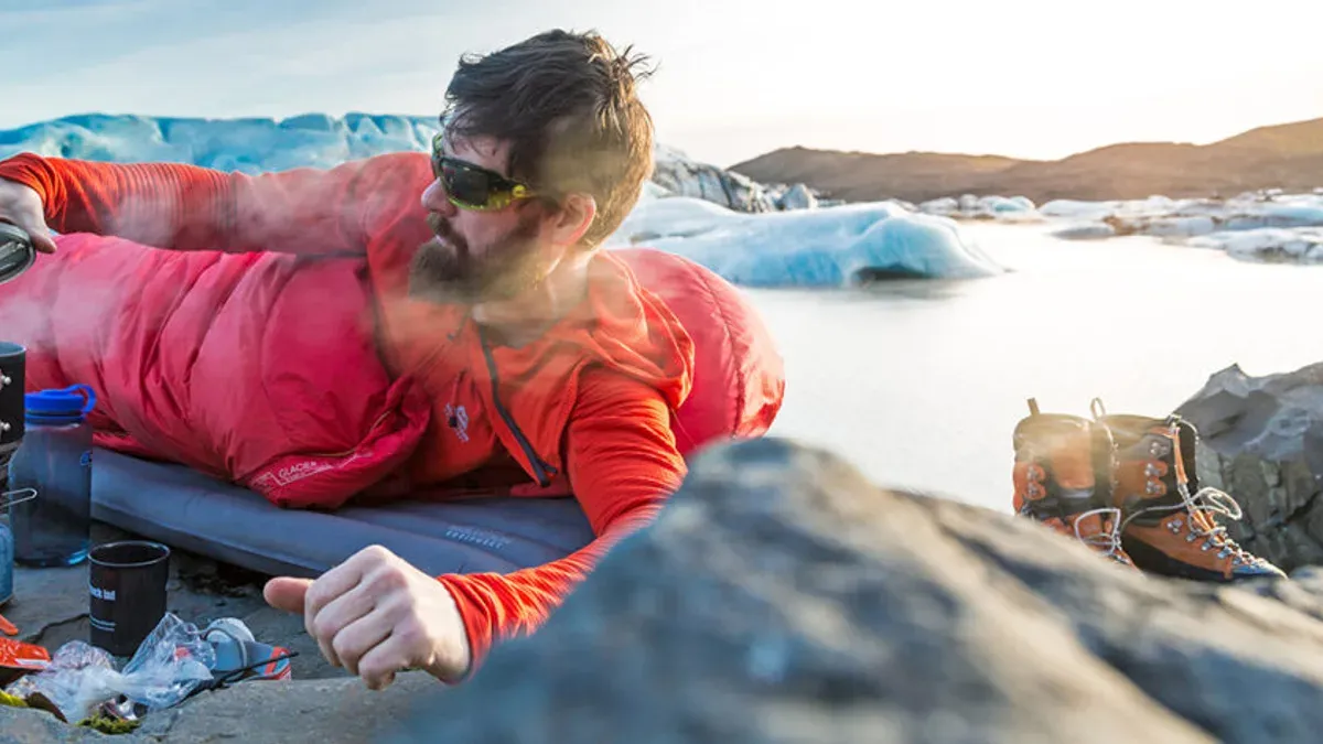 Man i röd vintersovsäck vilar vid isbelagd glaciärlagun
